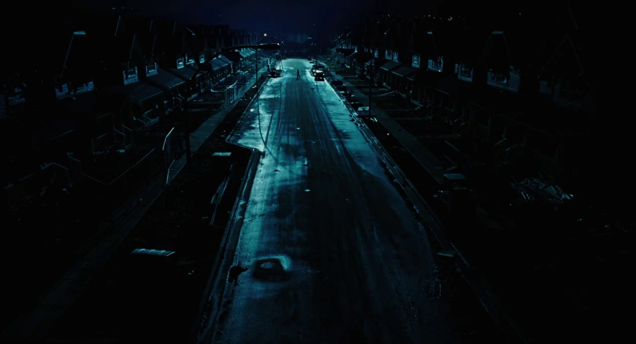 Jennifer’s Body (2009) movie still: establishing — A quiet suburban street at night is lined with dark, uniform residential houses. A single…