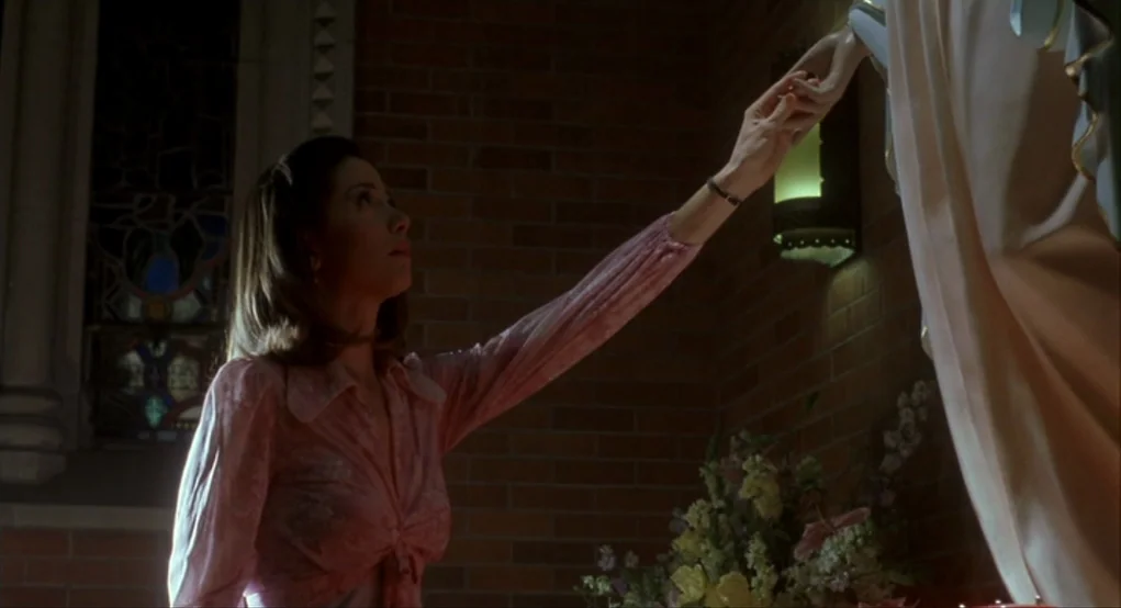 Summer of Sam (1999) movie still: medium — A dimly lit church corner features a red brick wall and stained glass windows. A woman reaches toward a…
