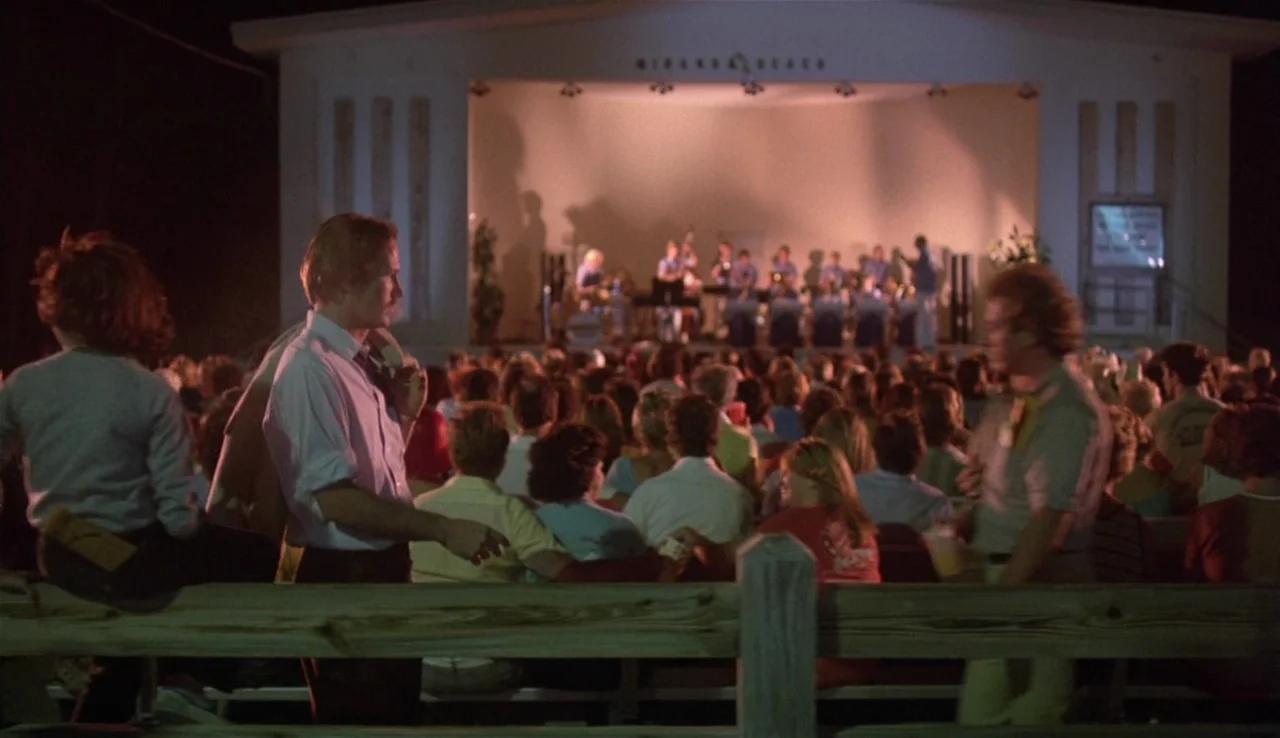 Body Heat (1981) movie still: wide — A crowd gathers at an outdoor band shell at night to hear a band. The man in the foreground stands by a…
