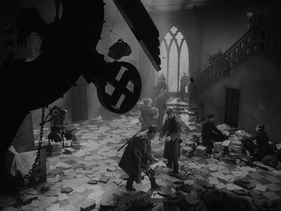 Ivan’s Childhood (1962) movie still: wide — A war-torn hall features scattered papers and debris beneath a massive hanging Nazi eagle. Soldiers in…