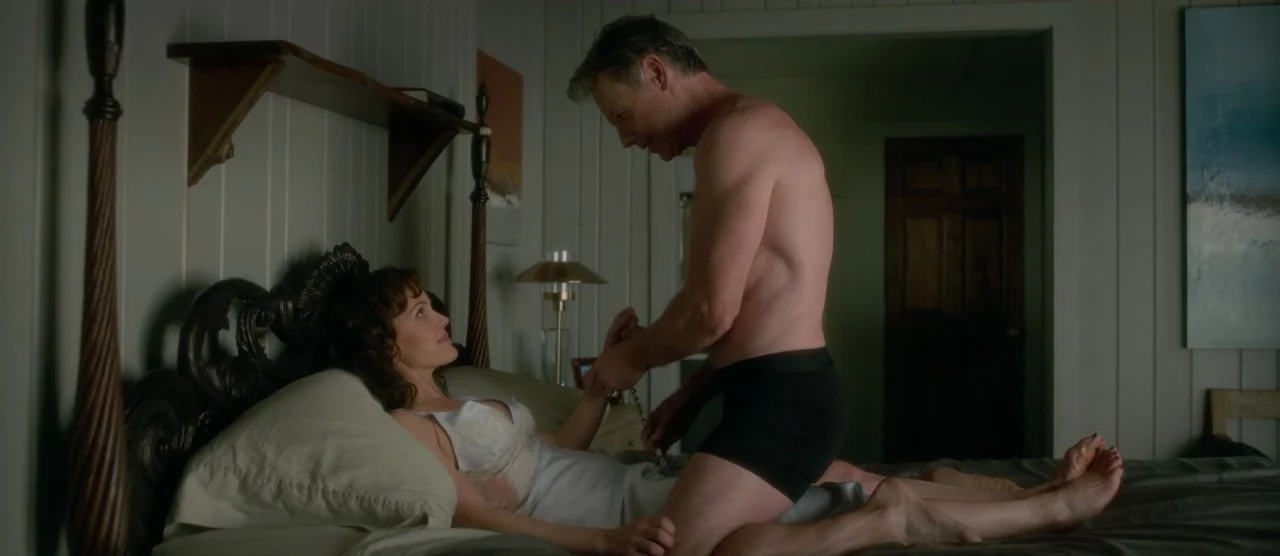 Gerald’s Game (2017) movie still: medium — A quiet bedroom features white vertical wooden paneled walls and a wooden bed frame. A man in black…