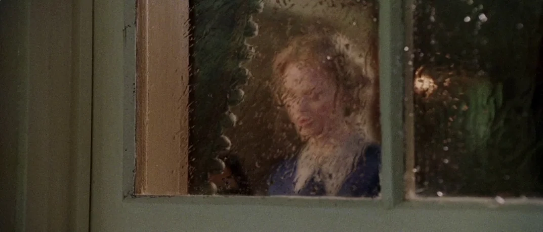 Cold Mountain (2003) movie still: medium — A woman stands behind a rain-streaked window pane of a wooden door. She looks into the dark interior…