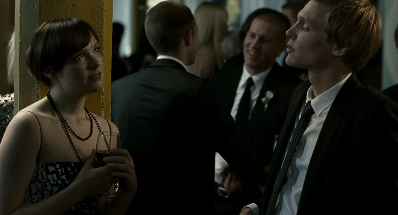 Reprise (2006) movie still: medium — A crowded indoor event with people in formal wear standing near a painted pillar. A woman with a drink and a…