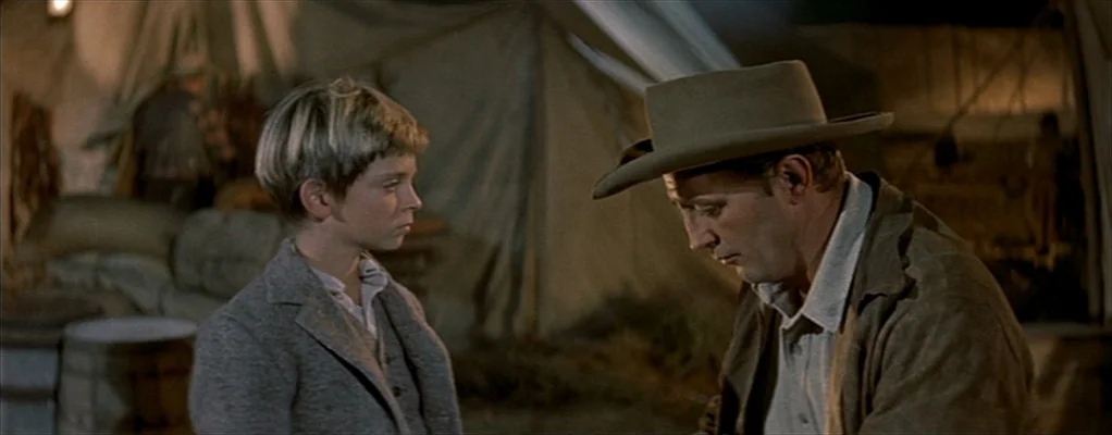 River of No Return (1954) movie still: medium — Two individuals stand outside a large canvas tent at night. The man in the cowboy hat looks down…
