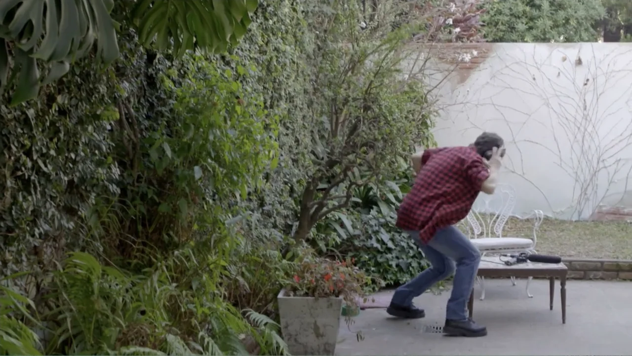 Heaven Sent (1994) movie still: fullbody — A residential patio features a dense ivy-covered wall and a concrete floor. A man wearing a red plaid…
