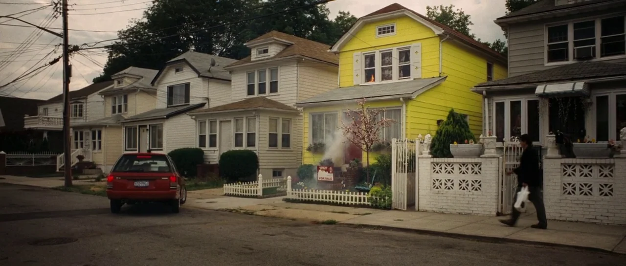 Synecdoche, New York (2008) movie still: wide — A residential street lined with suburban houses features one bright yellow residence. A man walks…