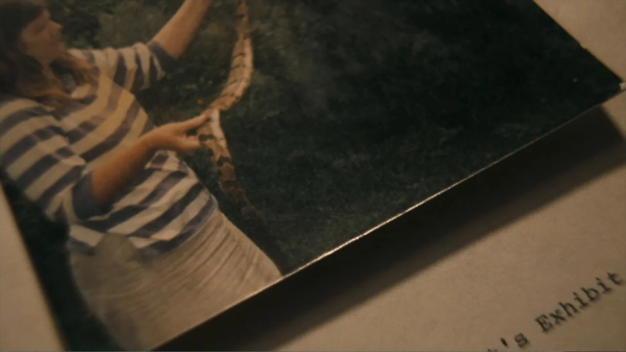 Alabama Snake (2020) movie still: closeup — A faded physical photograph lies on a flat surface with printed text nearby. The photograph depicts a…