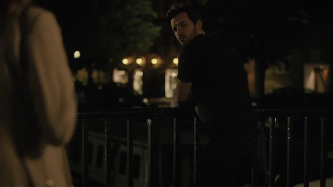 Copenhagen (2002) movie still: medium — A dark outdoor bridge at night with blurred background lights visible in the distance. A man stands at the…