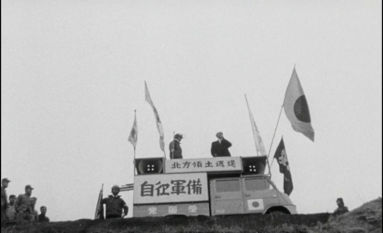 Sans Soleil (1983) movie still: wide — A boxy truck is parked atop a grassy ridge under a flat overcast sky. The vehicle is covered with Japanese…