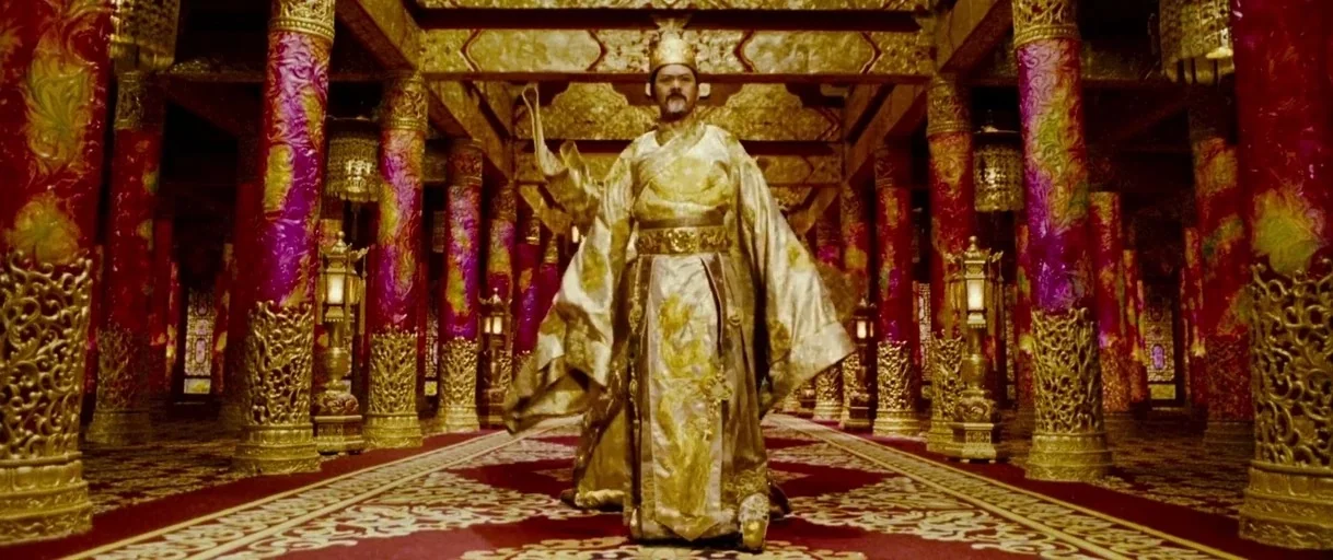 Curse of the Golden Flower (2006) movie still: fullbody — An expansive ornate hall features rows of polished purple pillars with gold dragon relief…