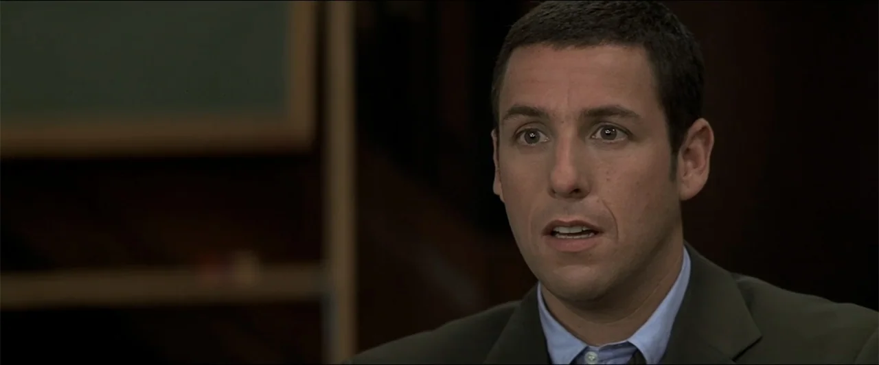 Anger Management (2003) movie still: closeup — A dark office environment with a muted green board visible in the background blur. A man in a suit…
