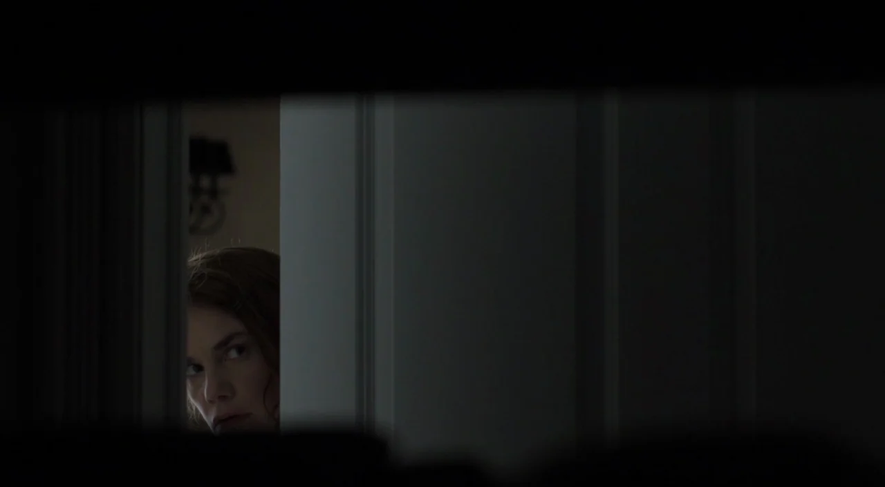 I Am The Pretty Thing That Lives In The House (2016) movie still: closeup — A woman looks through a narrow gap in a dark, partially opened door. The…