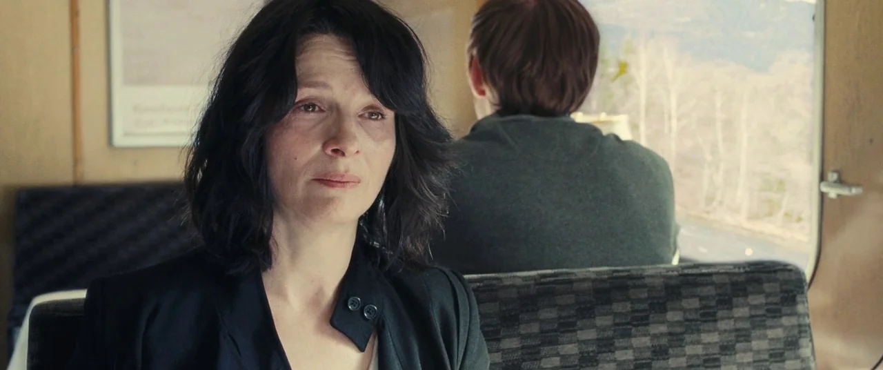 Clouds of Sils Maria (2014) movie still: medium — A passenger train cabin features patterned fabric seats and a window overlooking a landscape. A…