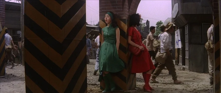 Gate of Flesh (1964) movie still: fullbody — A dusty outdoor marketplace features several wooden posts painted with black and yellow chevrons. Two…