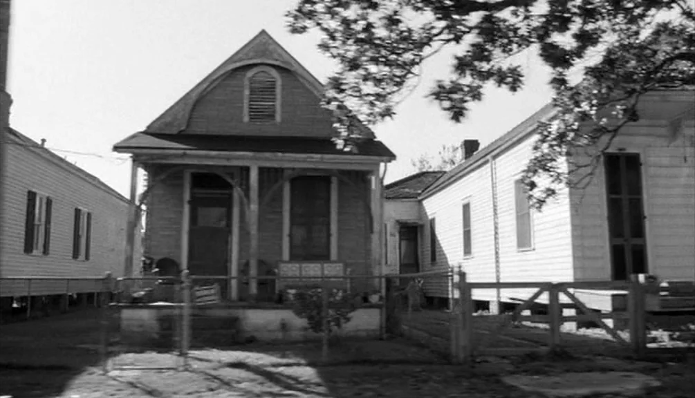 Down By Law (1986) movie still: establishing — A row of modest wooden shotgun-style houses features front porches and fenced yards. Tall trees…