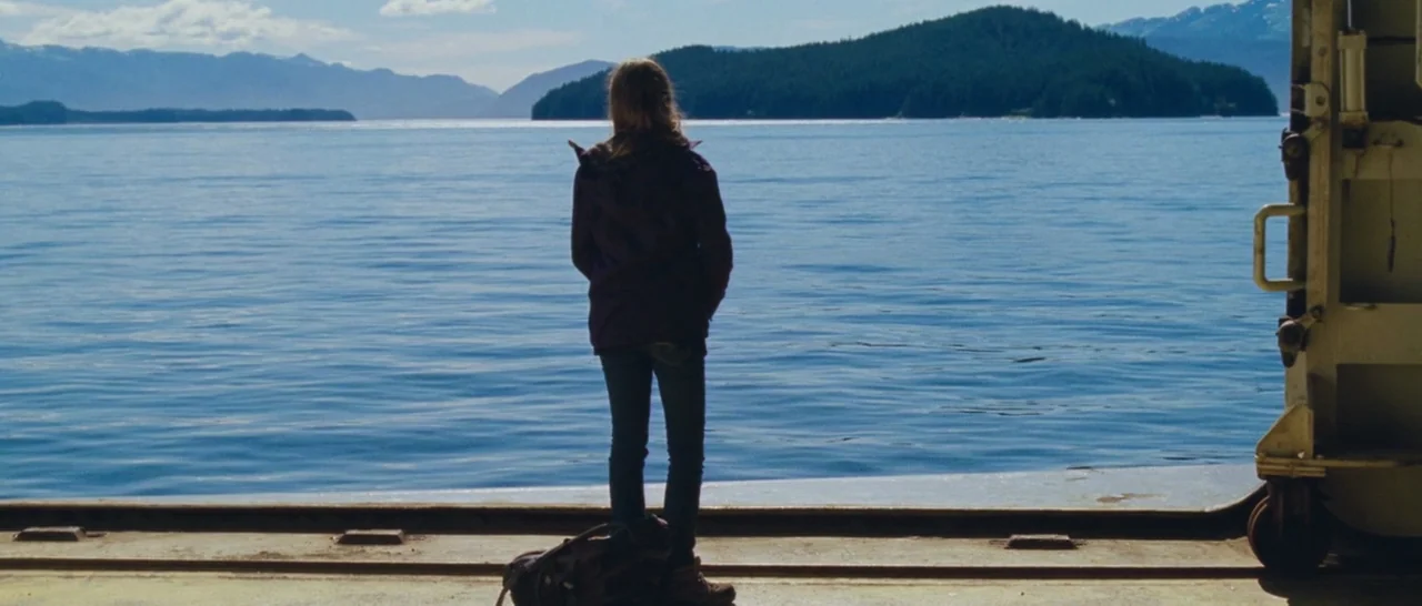Wildlike (2014) movie still: fullbody — An open deck of a ferry overlooks a large expanse of water and mountains. A lone individual stands at the…