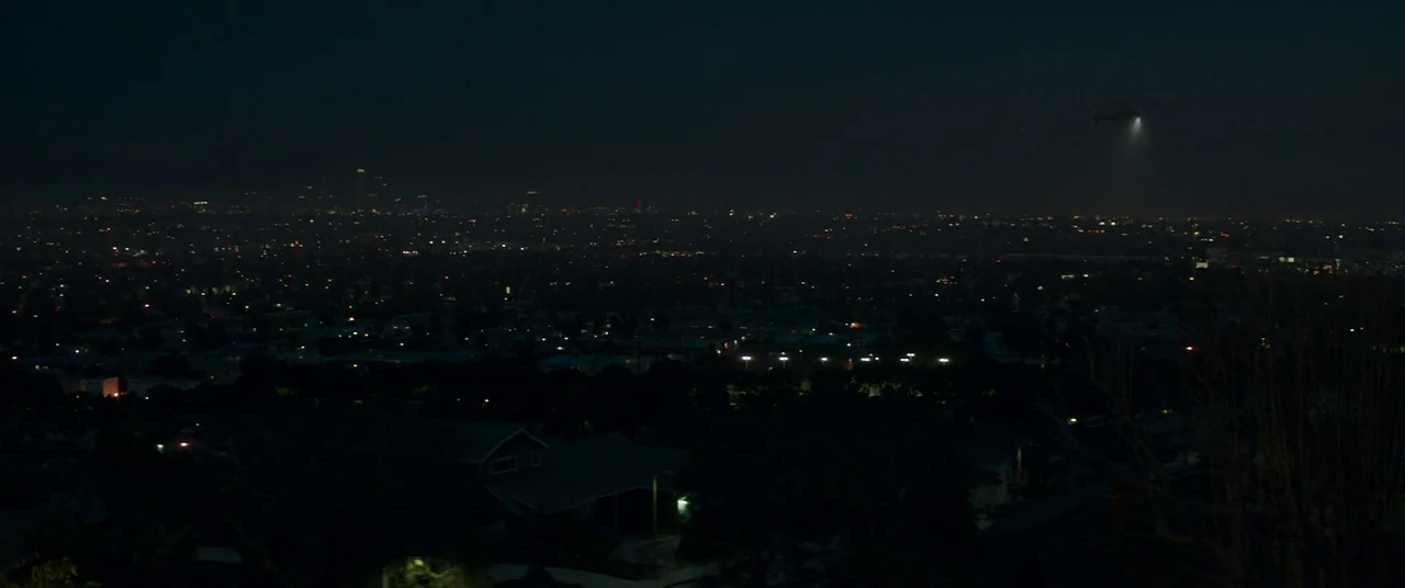 The Nice Guys (2016) movie still: establishing — A vast suburban sprawl stretches toward a distant illuminated high-rise city center at night. A…
