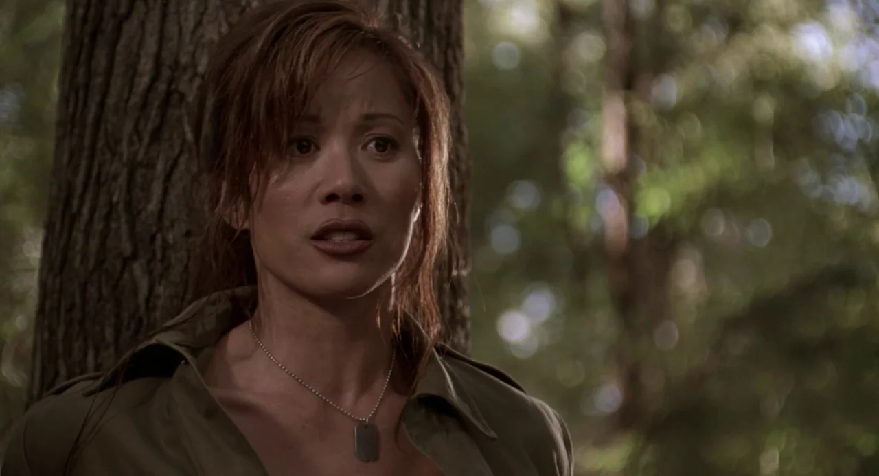 Universal Soldier: The Return (1999) movie still: closeup — A dense patch of trees creates a textured background with natural sunlight. A woman in a…