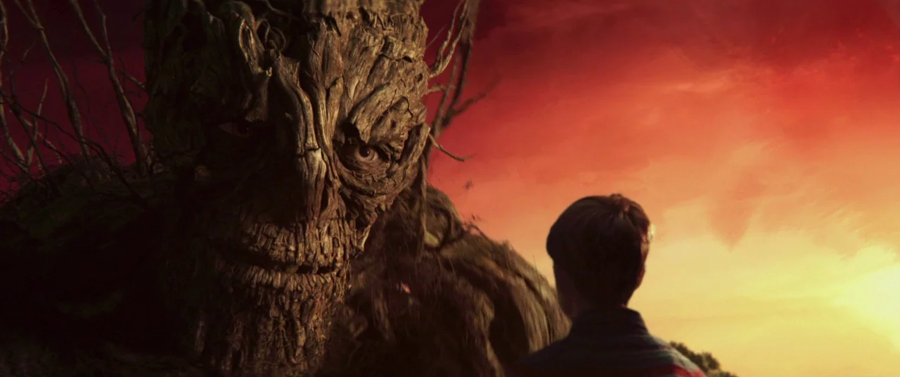 A Monster Calls (2016) movie still: medium — A field sits under a fiery orange sunset with dark clouds on the horizon. A young boy stands…
