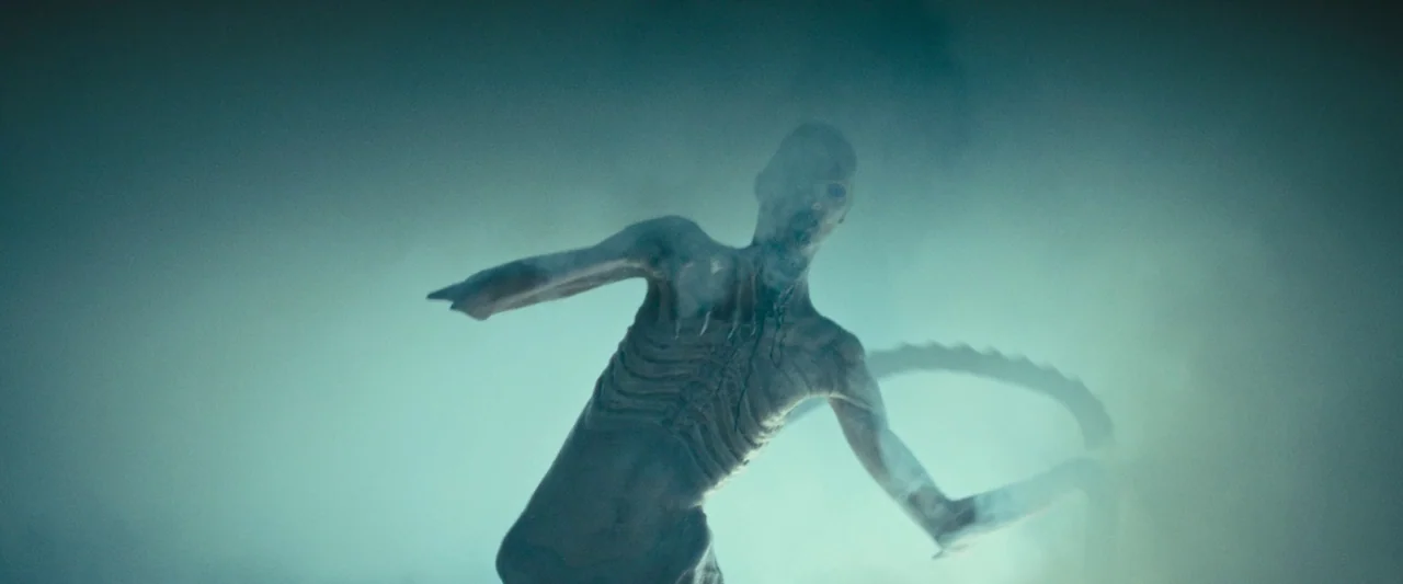 Alien: Romulus (2024) movie still: fullbody — A thick, hazy landscape filled with dense fog surrounds the solitary figure. The gaunt creature moves…