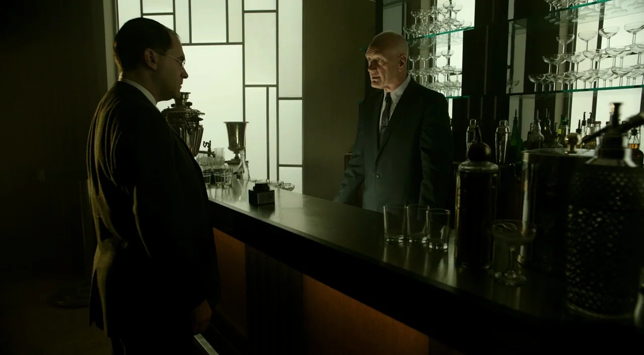 The Shape of Water (2017) movie still: medium — A dark indoor bar with a large geometric window grid in the back wall. Two men in suits stand on…