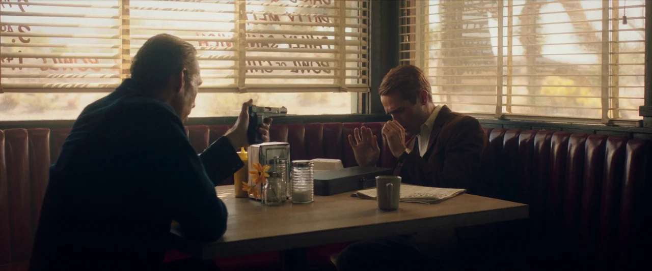 The Last Stop in Yuma County (2023) movie still: medium — A rustic diner booth features red vinyl upholstery and windows covered by venetian blinds.…