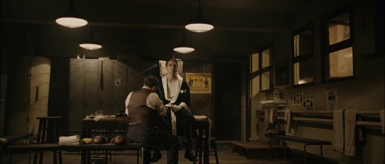 The Black Dahlia (2006) movie still: wide — A dark boxing gym locker room features industrial metal lockers and overhead light fixtures. A trainer…