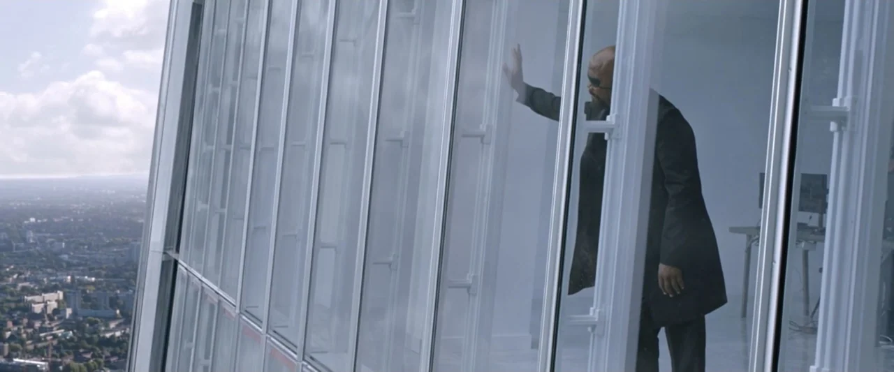 Spider-Man: Far From Home (2019) movie still: medium — A high-rise glass-walled office overlooks a distant sprawling cityscape under a cloudy sky. A…