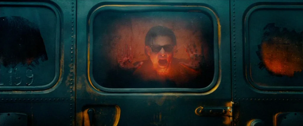 Hobo With A Shotgun (2011) movie still: medium — A man is trapped inside the window of a heavy, dark-painted metal vehicle. He presses his hands…