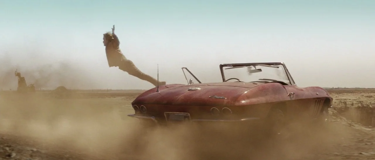 Star Trek (2009) movie still: wide — A dust-covered vintage red convertible drives across a flat, barren desert terrain. A man is suspended…