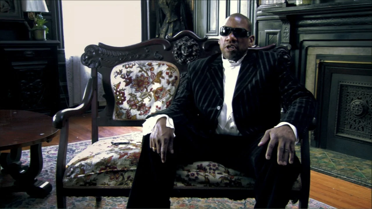 Dark Light: The Art of Blind Photographers (2009) movie still: medium — A dark parlor features an ornate wooden settee with floral upholstery placed…