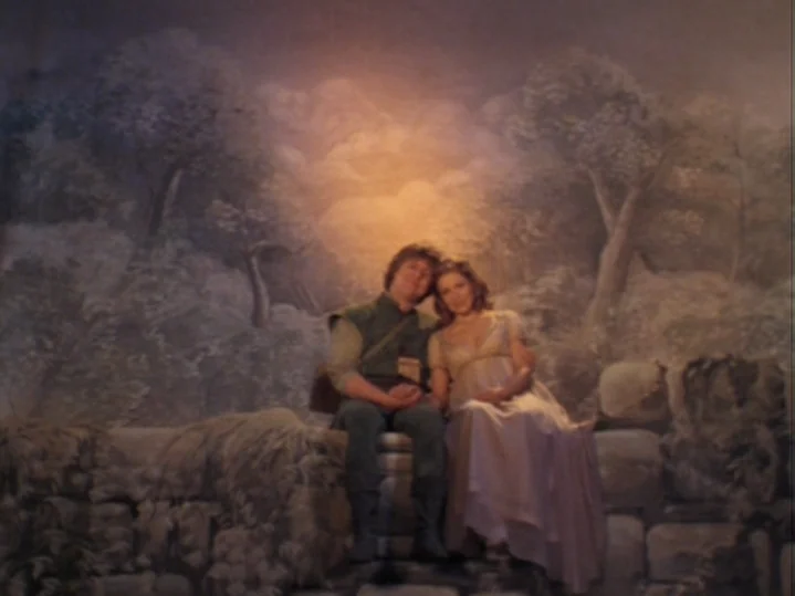 The Magic Flute (1975) movie still: fullbody — Two figures sit on a stone ledge in front of an intricate landscape mural. A man and a woman lean…