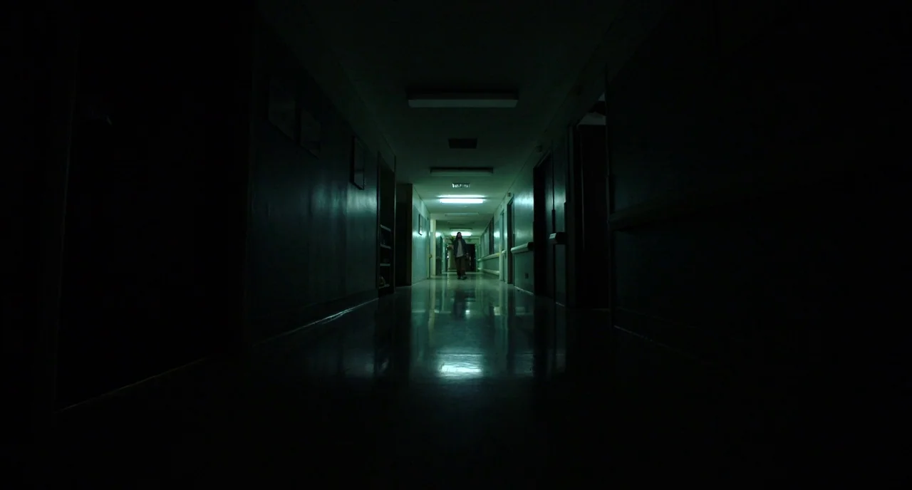 Nightmare Cinema movie still: wide — A dark hospital corridor features long shadows and reflective tile floors. A lone figure stands in the distant…