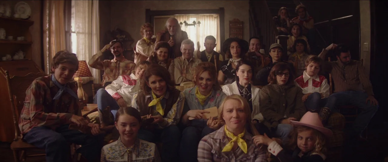 The Nowhere Inn (2020) movie still: wide — A crowded living room filled with family members seated on sofas and chairs. Everyone in the group stares…