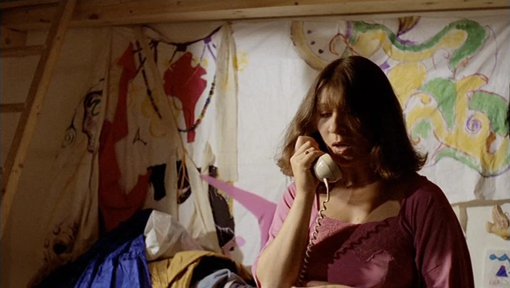 In A Year Of Thirteen Moons (1978) movie still: medium — A young woman stands inside a bedroom against a wall covered with painted sheets. She is…
