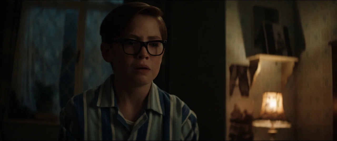 Rocketman (2019) movie still: medium — A dimly lit room with vintage patterned wallpaper features a small lamp and window. A young boy in pajamas…