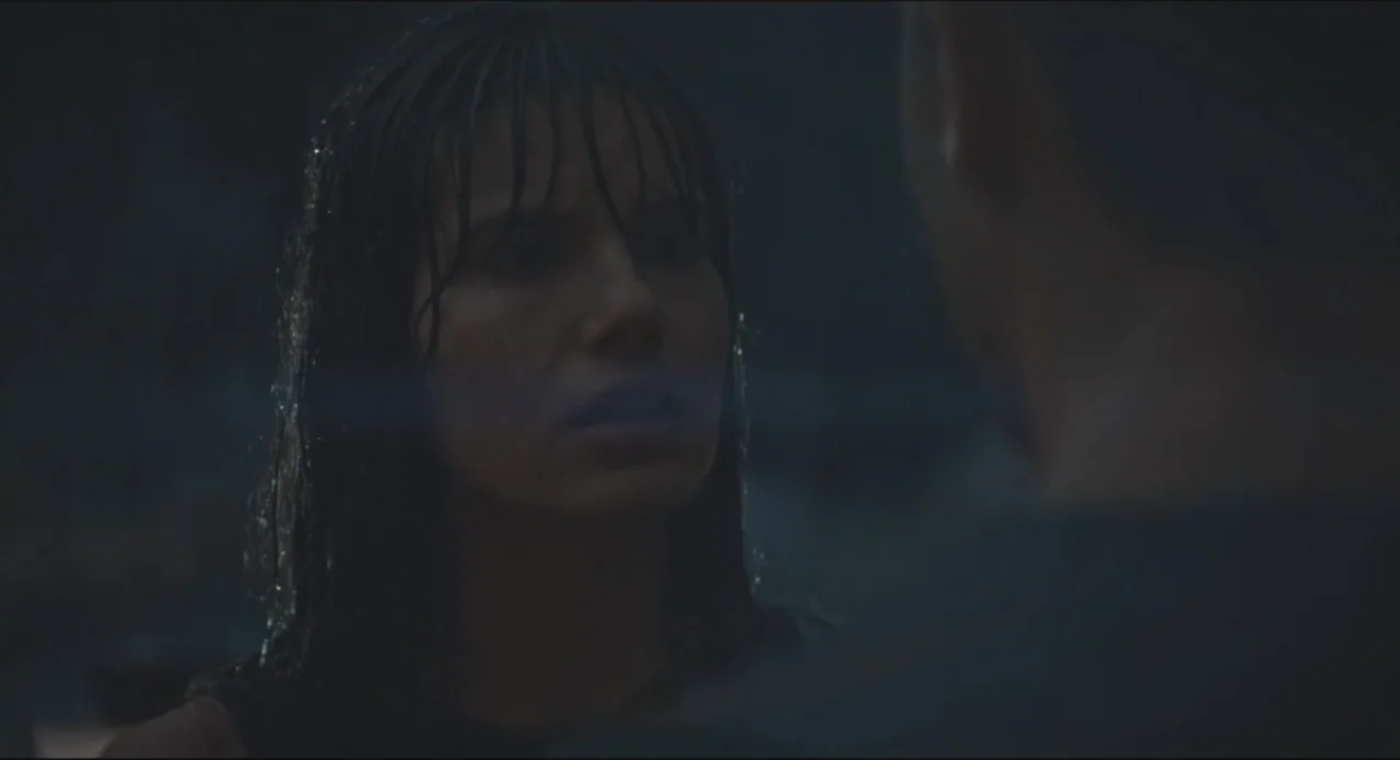 Proof of Love (2022) movie still: closeup — A dark, indistinct exterior area at night with low visibility. A woman with wet hair faces an unseen…