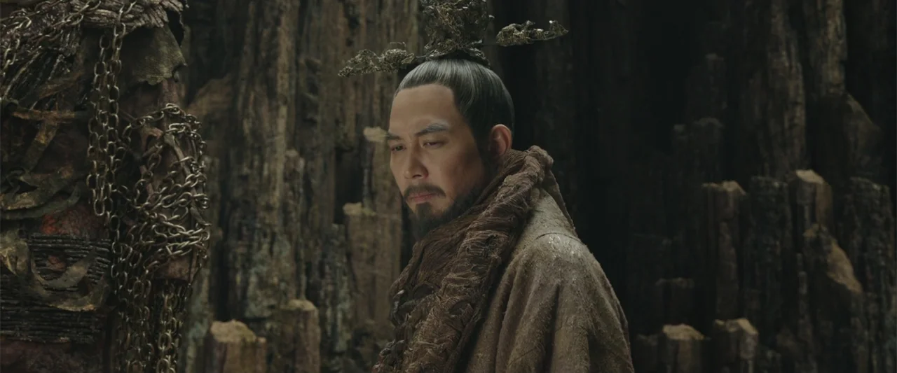 Along with the Gods: The Two Worlds (2017) movie still: medium — A man in traditional robes stands inside a dark, jagged stone cavern. The man gazes…