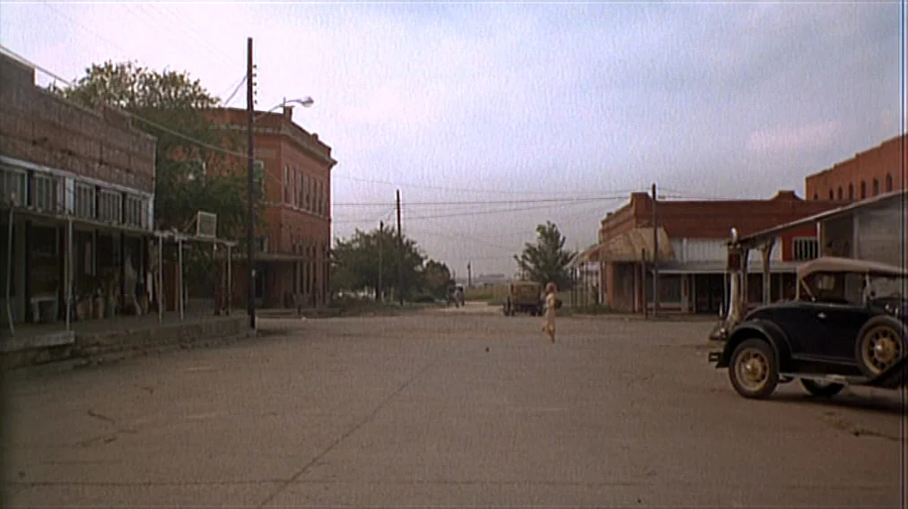 Bonnie And Clyde (1967) movie still: wide — An empty, dusty small town street is lined with weathered brick buildings. A solitary person walks…