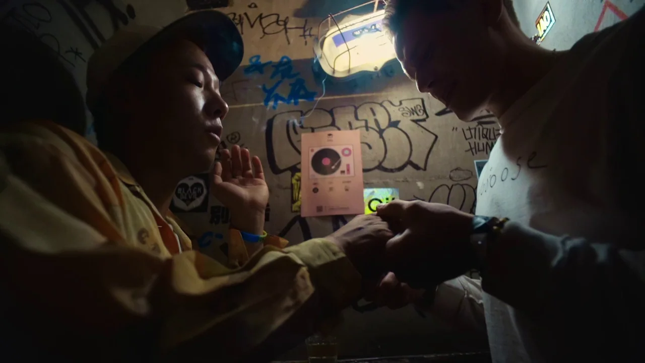 The Last Year of Darkness (2023) movie still: medium — A dimly lit room features walls covered in dark graffiti, stickers, and a vinyl record…