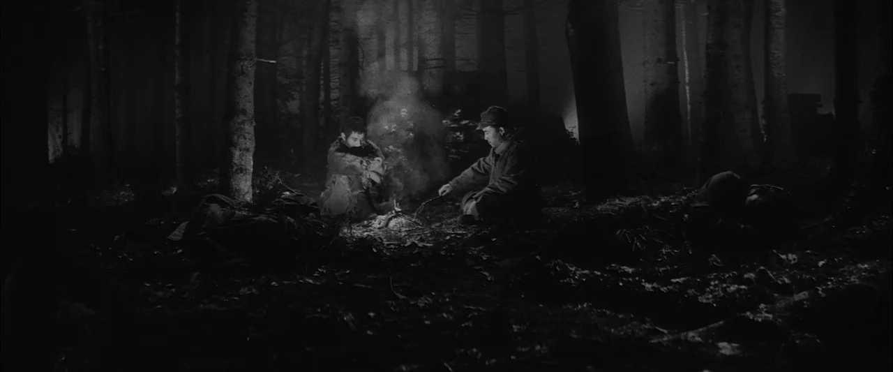 The Human Condition III: A Soldier’s Prayer (1961) movie still: wide — A dark, dense woodland area at night features tall silhouettes of trees. Two…