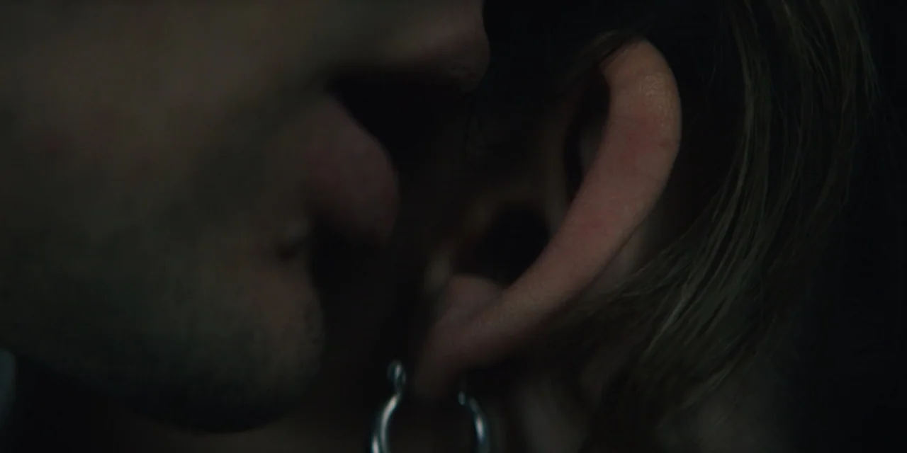 My Fault (2023) movie still: closeup — A very dark interior space where a person whispers near an ear. Only the side of a face and an ear with a…