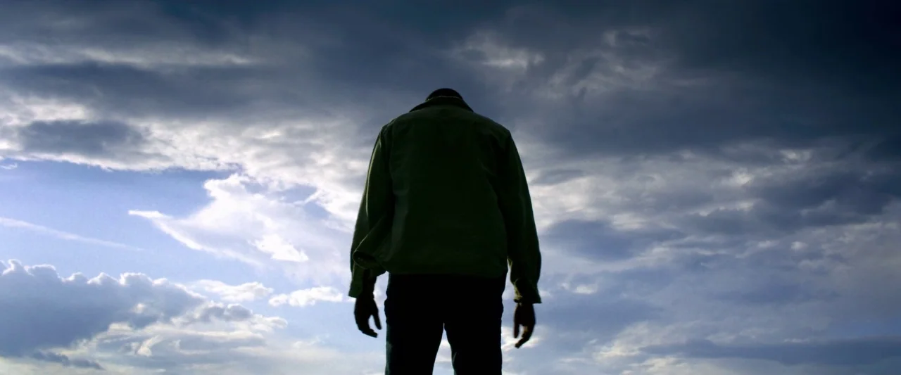 6 Underground (2019) movie still: fullbody — A vast, cloudy sky serves as the backdrop for a lone human figure. The individual stands facing away…