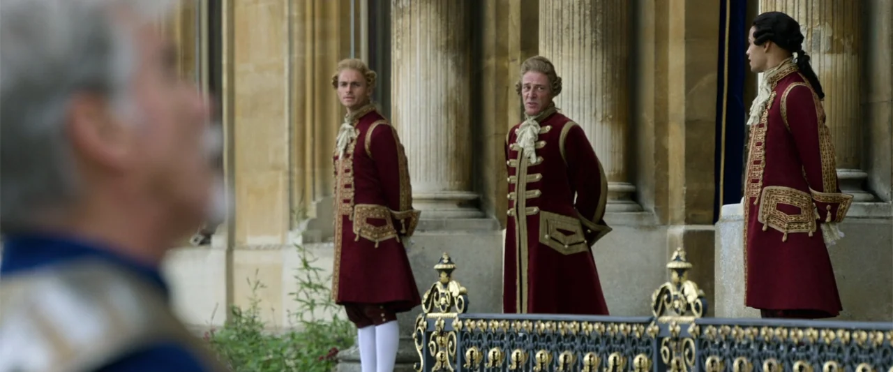 Cinderella (2015) movie still: medium — A stone courtyard features classical columns and an ornate wrought-iron railing in the foreground. Three men…