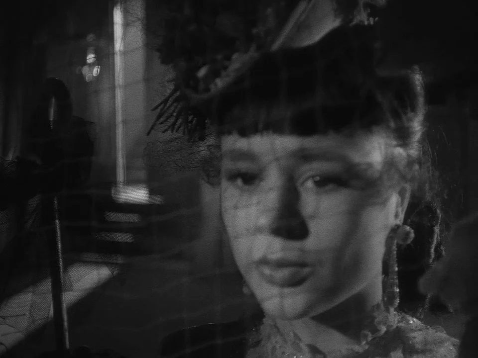 Sawdust and Tinsel (1953) movie still: closeup — A dimly lit room with a window visible in the blurred background. A young woman wears a lace veil…