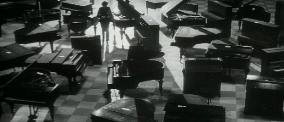 And The Fifth Horseman is Fear (1965) movie still: wide — A room packed with multiple upright and grand pianos on a checkered tile floor. A lone…