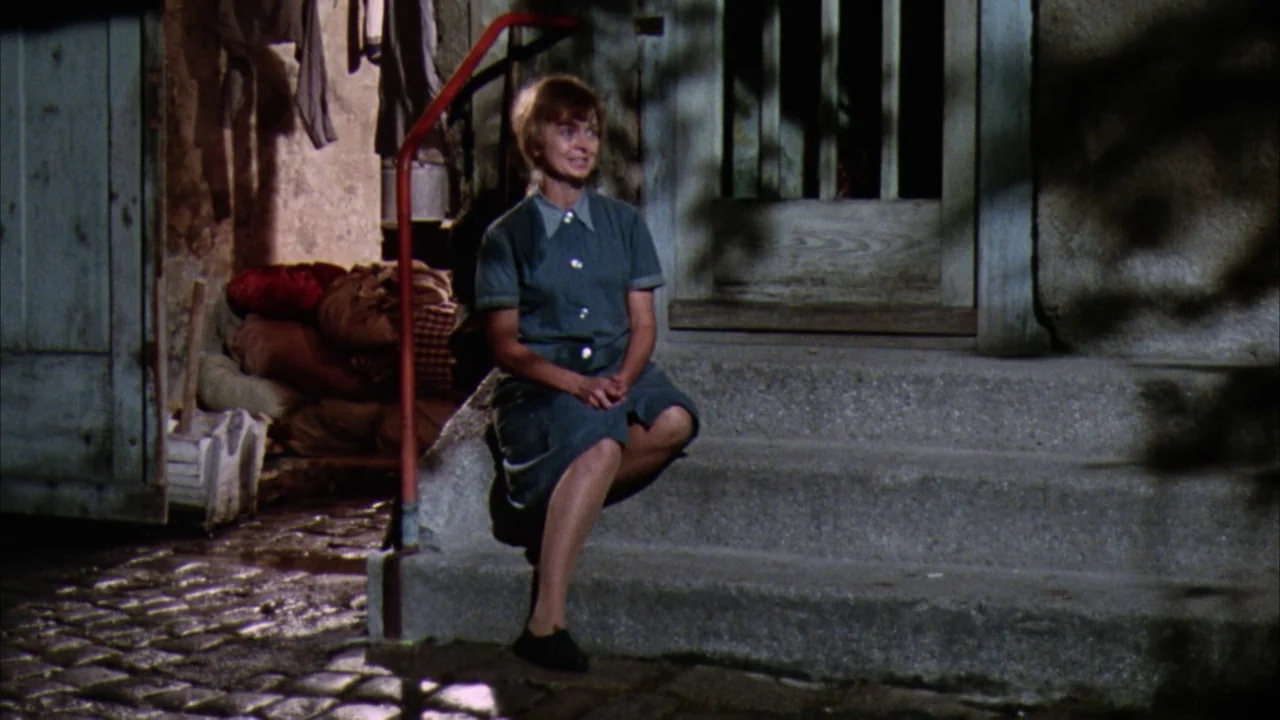 Willy Wonka & the Chocolate Factory (1971) movie still: fullbody — A woman sits on grey concrete steps outside a dark building at night. A red…