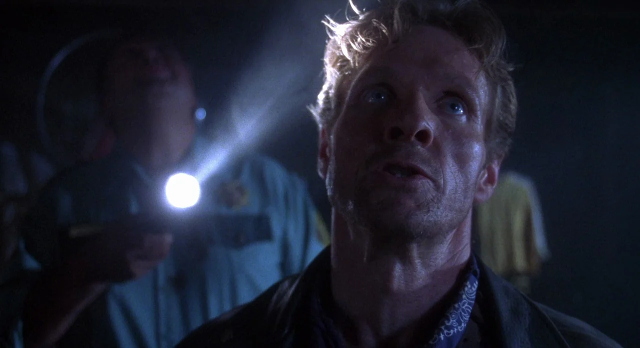Tales from the Crypt: Demon Knight (1995) movie still: medium — A dark, dimly lit environment where a beam of light cuts through the gloom. A man…