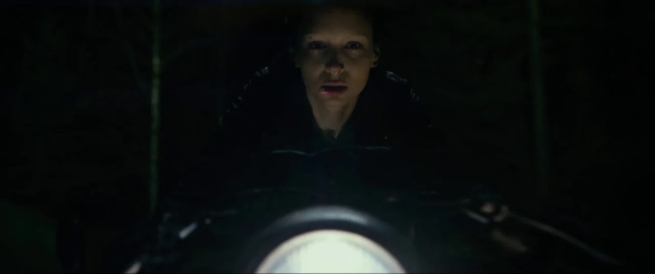 The Girl With The Dragon Tattoo (2011) movie still: medium — A motorcyclist rides along a dark path surrounded by dense, indistinct vegetation at…