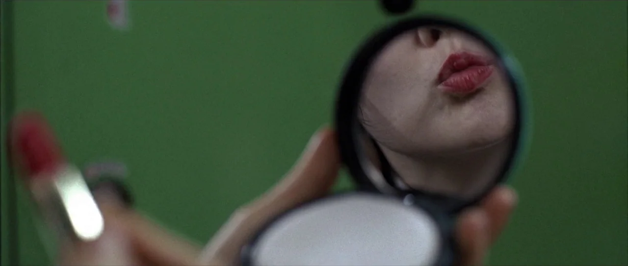 Lady Vengeance (2005) movie still: closeup — A green metallic surface acts as a backdrop for a small compact mirror. The reflection shows the lower…